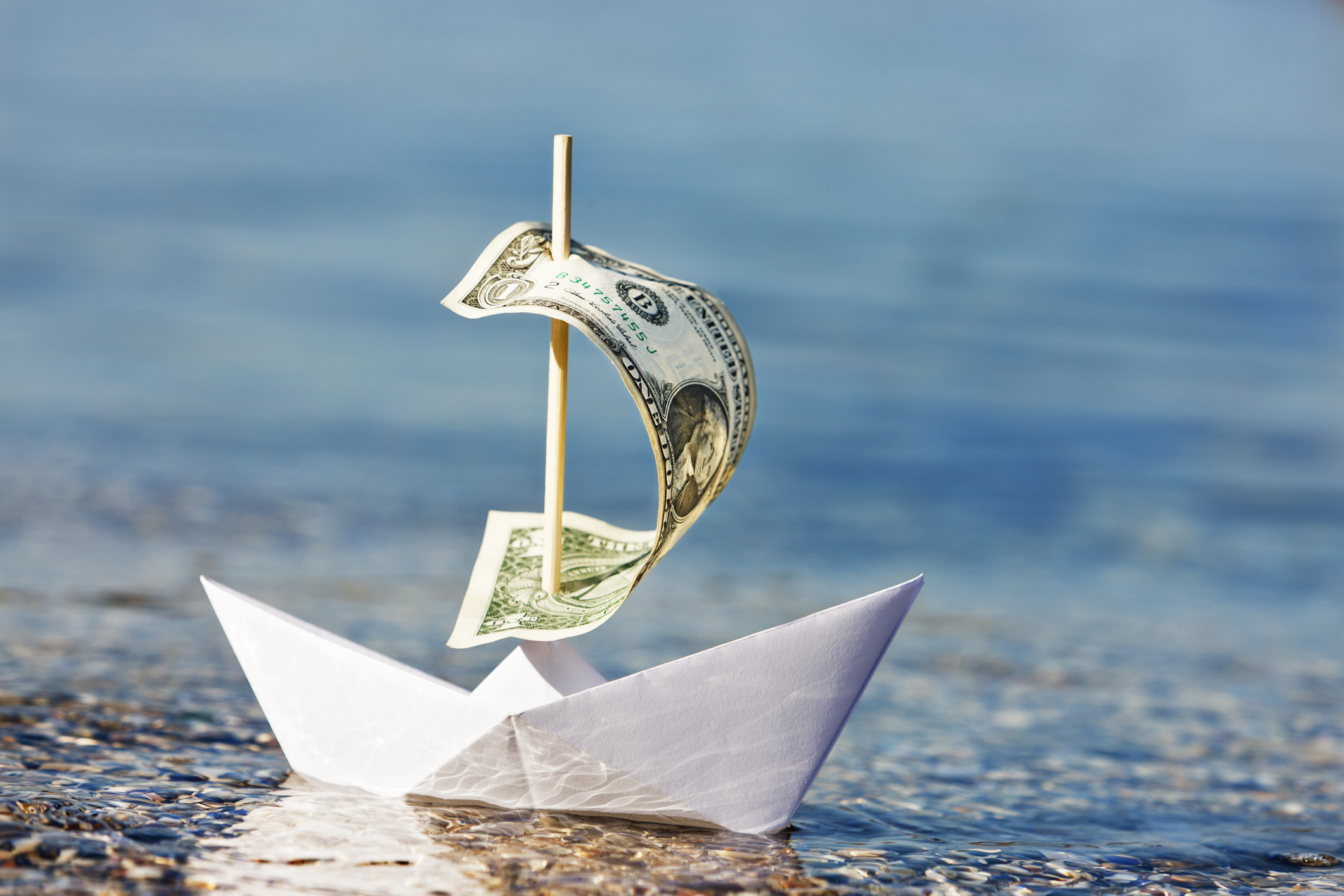 Paper boat with $1 bill sail is blown onshore